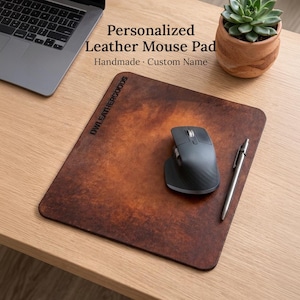 Peut inclure: Tapis de souris en cuir marron personnalisé avec le texte "Personalized Leather Mouse Pad Handmade Custom Name". Une souris noire et un stylo argenté sont posés sur le tapis. Un ordinateur portable est à côté.