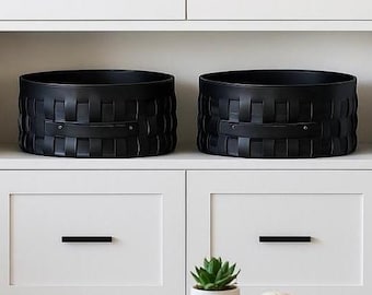 May include: A modern living room scene featuring white cabinetry with black hardware and two woven black storage baskets. A wooden coffee table holds a book, a small potted plant, and a decorative ball. A gray sofa with a decorative pillow is on the right.