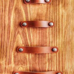 Peut inclure: Quatre lanières en cuir marron avec des boucles en métal argenté sont fixées à une surface en bois. Les lanières sont espacées uniformément et sont toutes de la même taille.