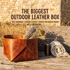 Könnte beinhalten: Eine braune Aufbewahrungsbox aus Leder mit sichtbaren Nähten, gefüllt mit getrocknetem Lavendel und gelben Blumen. Daneben stehen eine dunkle Metallflasche und ein gerollter cremefarbener Stoff. Der Text lautet: THE BIGGEST OUTDOOR LEATHER BOX 100% HANDMADE | GENUINE LEATHER | PERFECT FOR DECKS & PATIOS.