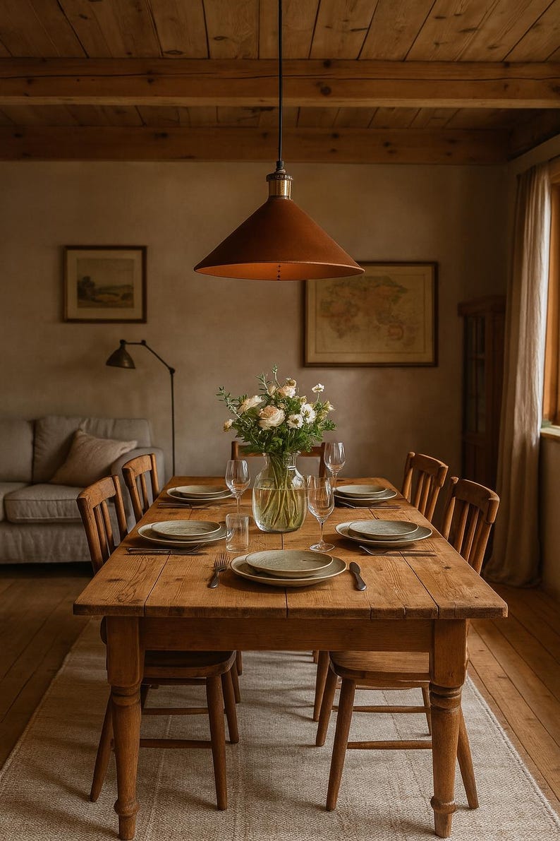 May include: A rectangular wooden dining table with six matching chairs, set with ceramic plates, silverware, and clear glassware. A glass vase filled with white and green flowers sits in the center, beneath a large, conical, copper-toned pendant light.