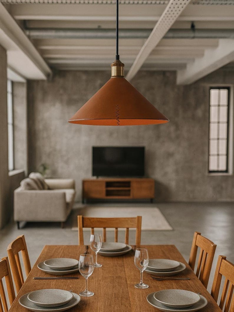 May include: A conical pendant light fixture with a smooth, matte brown exterior and a metallic brass-toned top fitting. The lamp is suspended by a thin black cord and features a visible vertical stitched seam detail along the side of the shade.