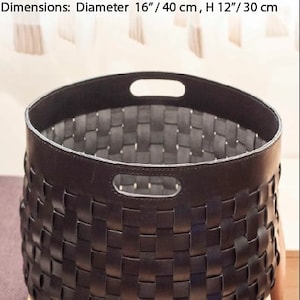 K&ouml;nnte beinhalten: Handgefertigter schwarzer Lederkorb mit gewebtem Design. Der Korb hat einen Durchmesser von 40 cm und eine H&ouml;he von 30 cm. Er hat zwei Griffaussparungen am Rand und ist aus pflanzlich gegerbtem Leder gefertigt.