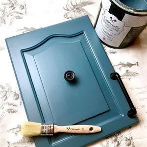 Peut inclure: Une porte de placard bleu sarcelle avec une poignée noire et une poignée en métal noir. La porte est peinte avec une finition de peinture vintage. Un pinceau et un pot de peinture sont également visibles sur l'image.