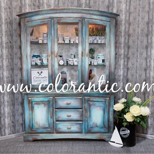 May include: A distressed turquoise blue hutch with glass doors and drawers. The hutch is filled with various jars and bottles of paint. The website www.colorantic.com is displayed on the front of the hutch.