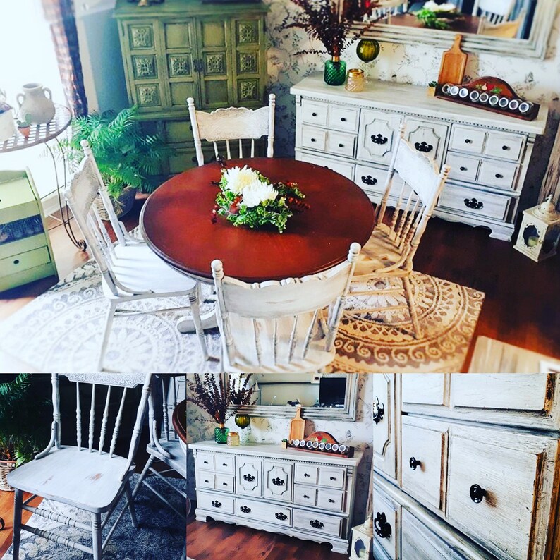May include: A white, distressed wood dining table set with four chairs. The table has a round, brown top and the chairs have white painted wood frames. The table is set with a bouquet of white flowers in the center.