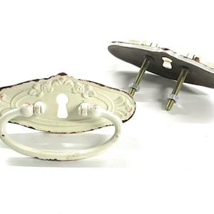 May include: Two white metal drawer pulls with a keyhole design and a distressed finish. Each pull has a loop handle and comes with two screws.