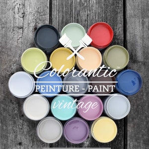May include: A collection of 14 paint jars in various colors, including green, blue, yellow, red, and white. The jars are arranged in a circle on a wooden surface. The text "Colorantic&trade; PEINTURE - PAINT vintage www.colorantic.com" is visible in the center of the image.