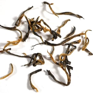May include: Loose black tea leaves with golden tips. The tea leaves are curled and twisted, and some are broken.
