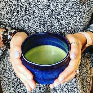 Puede incluir: Una persona sosteniendo una taza de cer&aacute;mica azul llena de t&eacute; matcha verde.