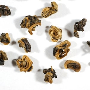 May include: Loose leaf black tea with golden tips, also known as golden needle tea, in various shapes and sizes. The tea leaves are a mix of brown and gold colors.