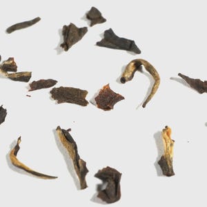 May include: A collection of loose dried tea leaves scattered across a plain surface. The leaves vary in color from dark brown and black to lighter tan and golden hues, featuring curled, twisted, and fragmented shapes of various sizes.