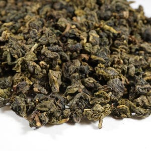 May include: Close-up of loose leaf green tea, with a dark green color and a slightly curled shape.