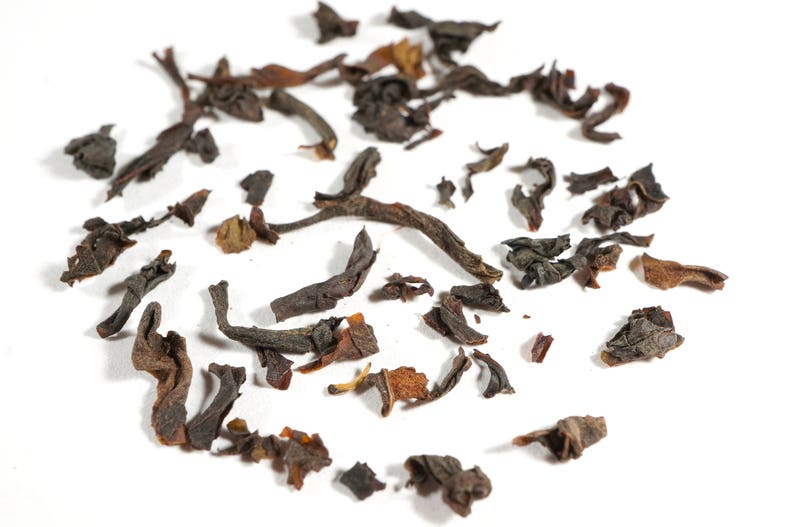 May include: Loose black tea leaves scattered on a white surface. The leaves are dry and have a dark brown color.