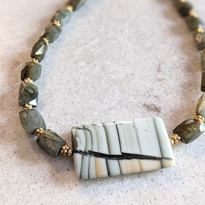 May include: A necklace made of green and gold beads with a large rectangular pendant made of white and black patterned stone.