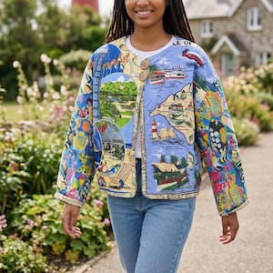 May include: A long-sleeved, quilted jacket featuring a vibrant, multi-coloured collage print of coastal scenes, maps, and marine life. The jacket has a round neckline, two large wooden buttons at the top, and a light-coloured trim along the edges.