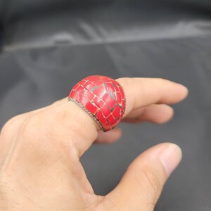 Puede incluir: Un anillo de mosaico rojo con una banda plateada. El anillo est&aacute; hecho de peque&ntilde;os cuadrados rojos que est&aacute;n engastados en una banda plateada.