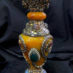 Op de afbeelding: Een gele ambervaas met ingewikkelde zilveren en gouden metaalbewerking en kleurrijke edelsteenaccenten.