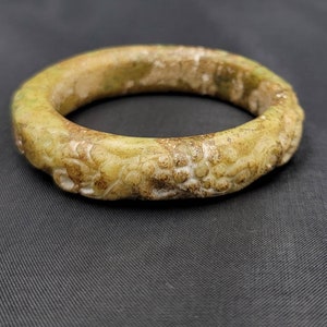 May include: A pale green jade bangle with intricate carvings. The bangle is smooth and polished, with a slightly worn appearance.