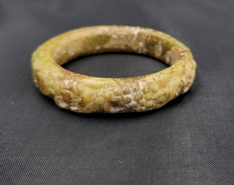 May include: A pale green jade bangle with intricate carvings. The bangle is smooth and polished, with a slightly worn appearance.
