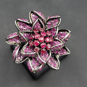 Może przedstawiać: Srebrny pierścionek z wzorem różowej róży. Kwiat wykonany jest z małych różowych kamieni szlachetnych i ma srebrne centrum.