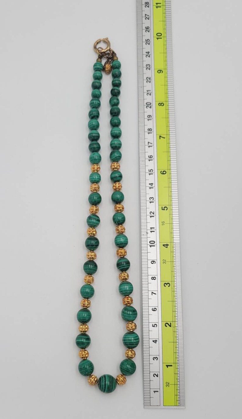May include: A green malachite bead necklace with gold accents. The necklace is approximately 18 inches long and features a clasp closure.