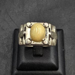 Może przedstawiać: Srebrny pierścionek z dużym, owalnym, jasnożółtym kamieniem szlachetnym osadzonym w misternym, ozdobnym wzorze.