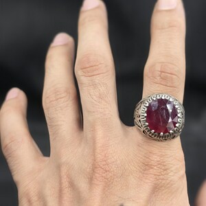 May include: A silver ring with an ornate design and a large, oval-shaped ruby gemstone.