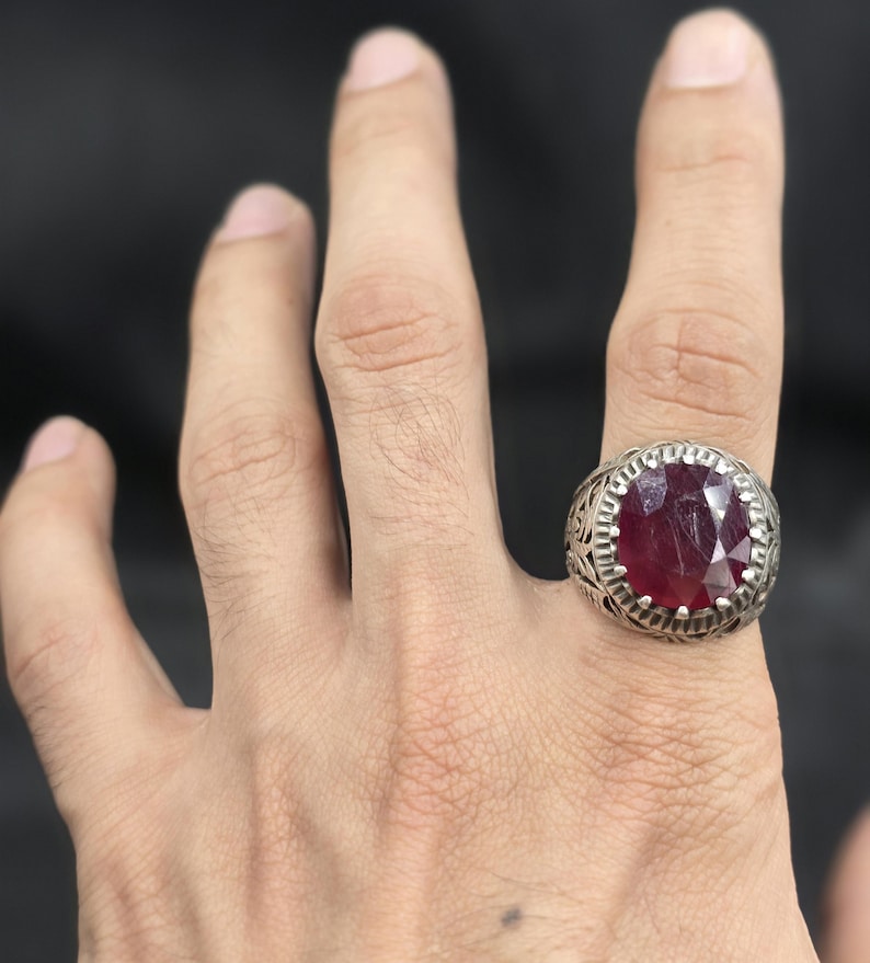 May include: A silver ring with an ornate design and a large, oval-shaped ruby gemstone.