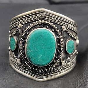 Könnte beinhalten: Ein silbernes Armband mit komplizierten Designs und Türkis-Steinen. Das Armband ist breit und hat eine gebogene Form.