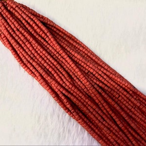 May include: A bundle of small, cylindrical beads in a reddish-orange hue. The beads are tightly strung together, creating a dense, textured appearance. The beads are likely for jewelry making or other craft projects.
