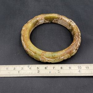 May include: A green jade bangle with a carved floral design. The bangle is approximately 2.5 inches in diameter.