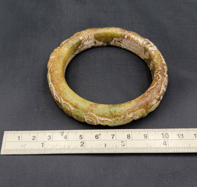 May include: A green jade bangle with a carved floral design. The bangle is approximately 2.5 inches in diameter.