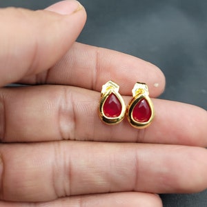 Puede incluir: Un par de pendientes de oro con piedras rojas en forma de lágrima.