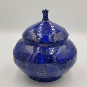 Op de afbeelding: Een blauwe lapis lazuli decoratieve doos met een deksel. De doos is gemaakt van kleine, ingewikkeld gesneden stukjes lapis lazuli, waardoor een mozaïekpatroon ontstaat.