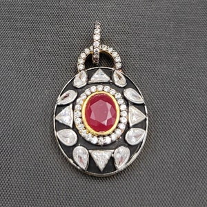May include: A silver pendant with a black enamel oval setting. The pendant features a red gemstone surrounded by clear gemstones. The pendant has a silver bail.