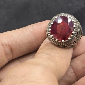 May include: A silver ring with an ornate design and a large, round, red gemstone.