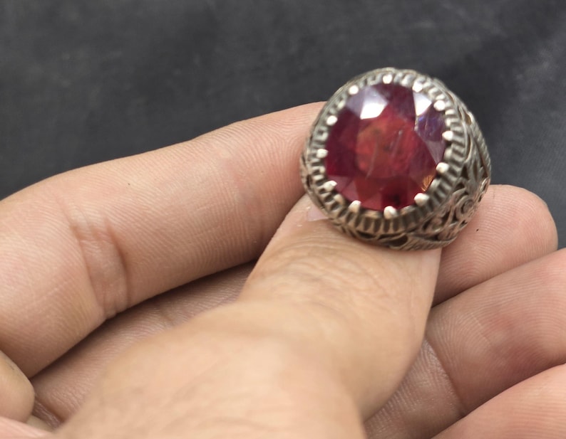 May include: A silver ring with an ornate design and a large, round, red gemstone.