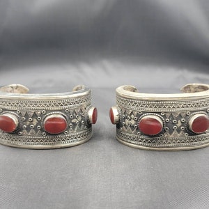 May include: A pair of silver bracelets with intricate designs and red gemstone accents.