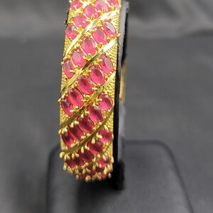May include: A gold bangle bracelet with a design of pink oval-shaped gemstones set in a gold frame.