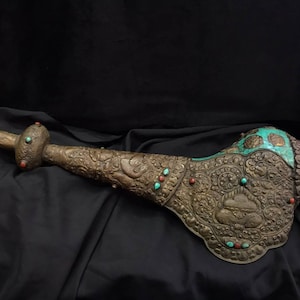 Puede incluir: Un cuerno de caracola decorativo con tallas intrincadas y piedras preciosas turquesa y rojas. El cuerno está hecho de metal y tiene una forma larga y curva.