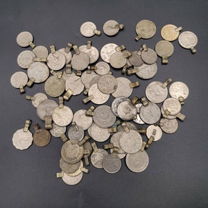 May include: A collection of silver-toned metal charms with various designs, including floral patterns, geometric shapes, and abstract motifs. The charms are arranged in a random pattern on a dark grey surface.