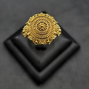 Könnte beinhalten: Ein goldener Ring mit einem runden Design, das mit komplizierten Details und einer strukturierten Oberfläche verziert ist.