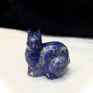 Peut inclure: Une petite figurine de chat en lapis-lazuli bleu sculpté avec des yeux dorés. Le chat est assis, la tête légèrement inclinée sur le côté.