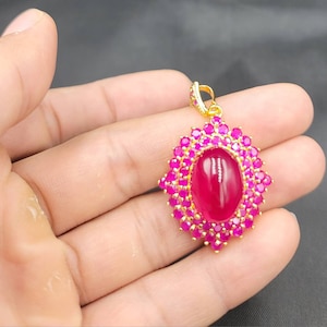 May include: A gold pendant with a large oval-shaped pink gemstone surrounded by smaller pink gemstones.