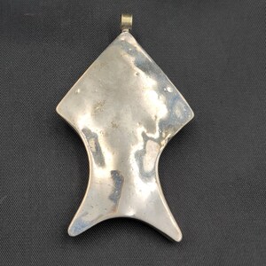 May include: A silver pendant in the shape of a stylized fish with a loop at the top for attaching a chain.