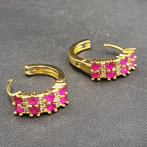 Könnte beinhalten: Ein Paar goldene Creolen mit pinkfarbenen und weißen Zirkonia-Steinen. Die Ohrringe sind in einem schlichten und eleganten Design gehalten.