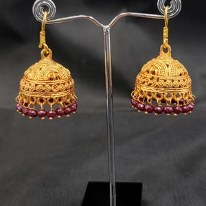 May include: A pair of gold earrings with a decorative design and burgundy beads hanging from the bottom.
