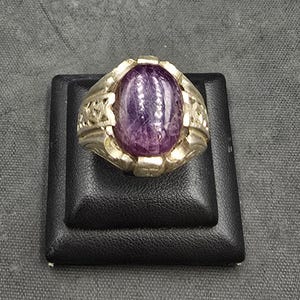 May include: A silver ring with an ornate design and a large, oval-shaped purple gemstone.