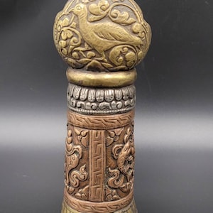 May include: A decorative, ornate, cylindrical, gold and silver, metal seal with a bird design on the top.